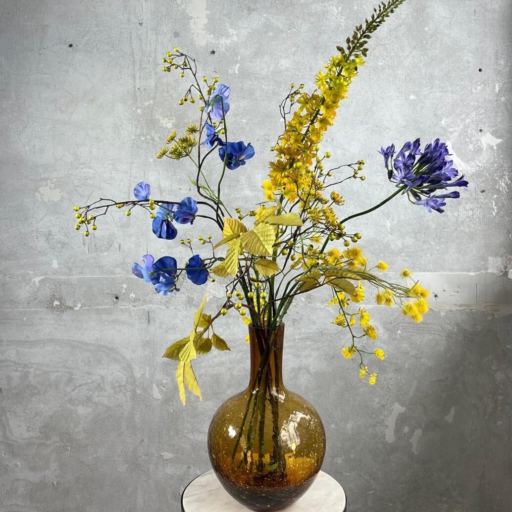 'n Zijden bloemen boeket in prachtig geel met blauwe accenten. Een mooi, vrolijk en zonnig geheel. Een ware eyecatcher in iedere ruimte. Met blauwe Lathyrus, gele Dille, gele bessen, blauwe Agapanthus en geel/oranje Eremurus. De Eremurus, wordt ook wel naald van Cleopatra genoemd.