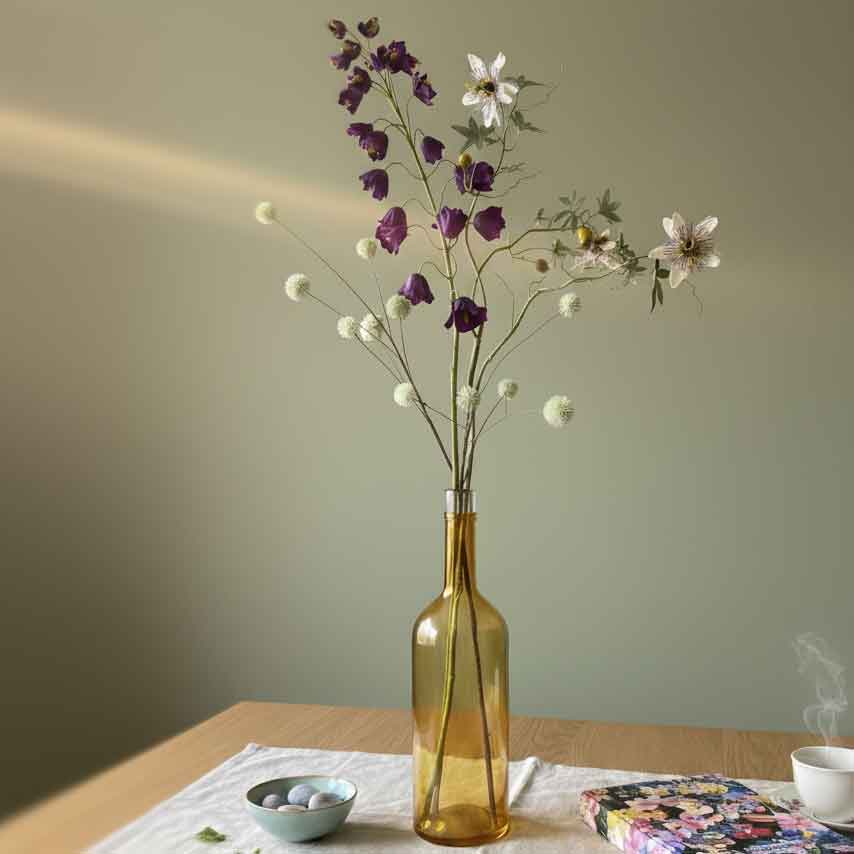 Kunstbloemen combitip met passiebloem, frittilaria en distel in gouden glazen vaas op houten tafel in modern interieur