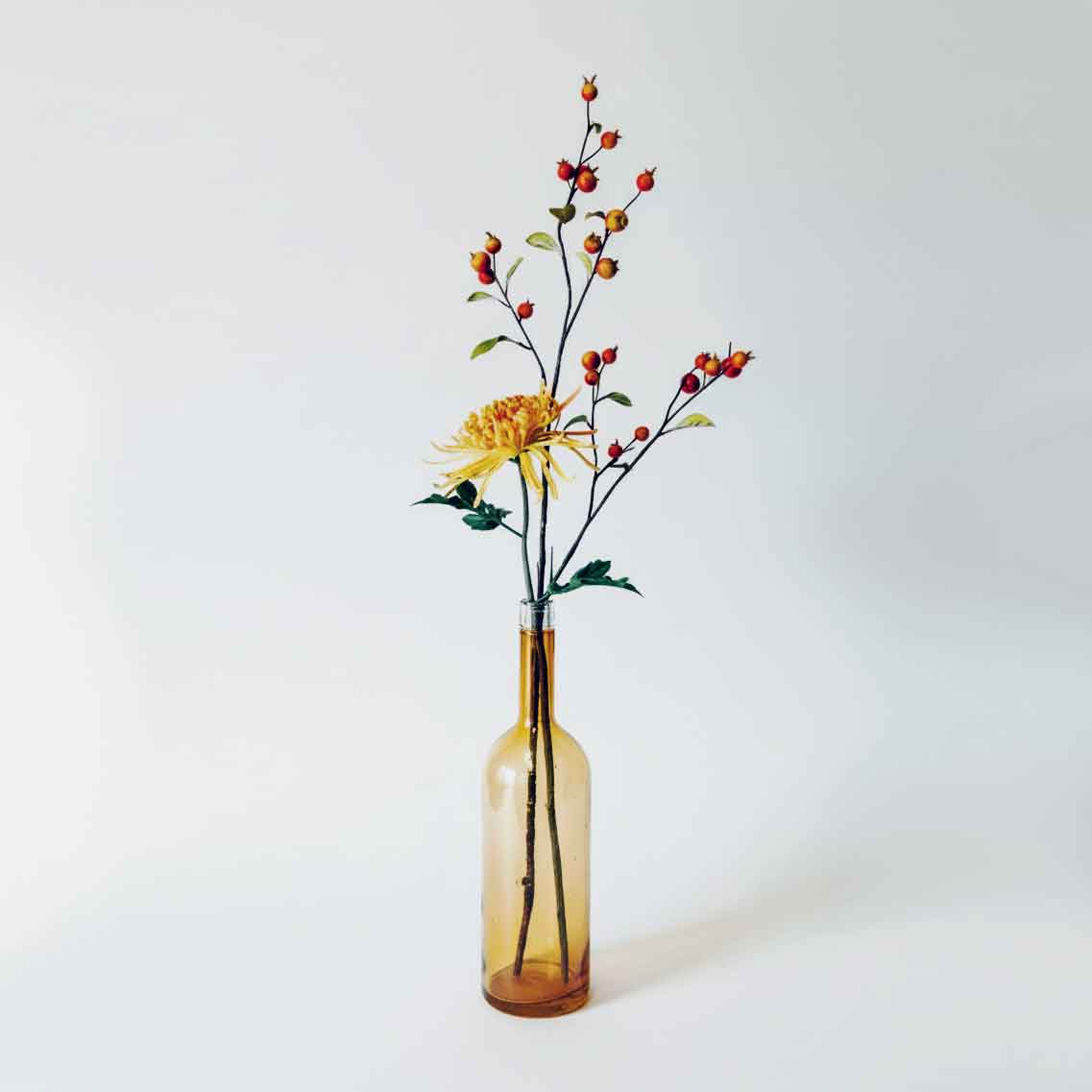 Kunstbloemen combitip met gele spin chrysant en rozenbottels in amber glazen vaas