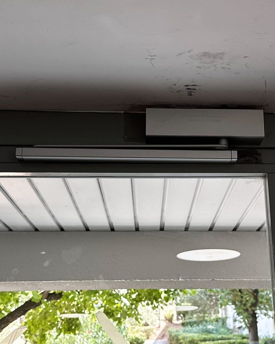 Bandeau ventouse électrique et ferme-porte posés en haut d’une porte de hall