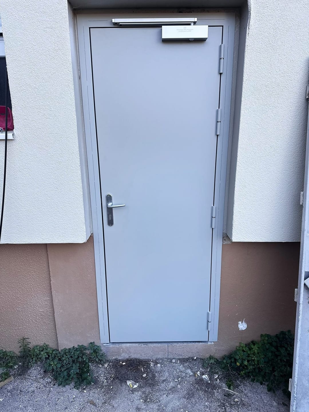 Porte métallique grise d’accès aux caves, avec ferme-porte