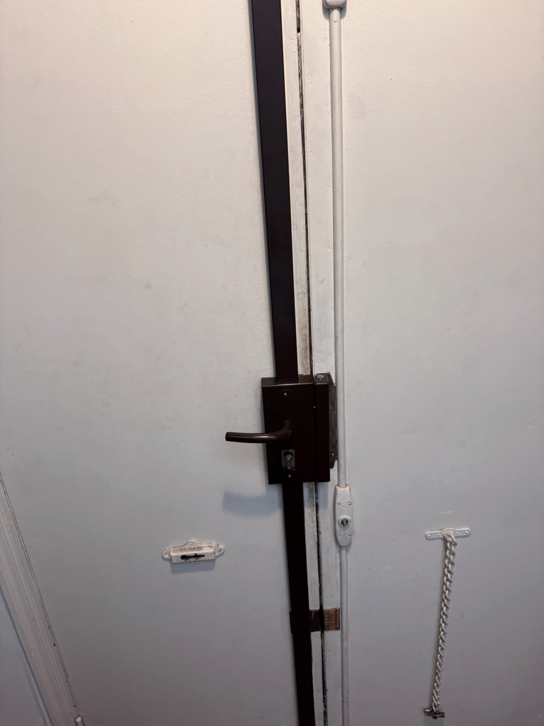Serrure multipoints en applique avec ses tringles, posée sur une porte d’appartement