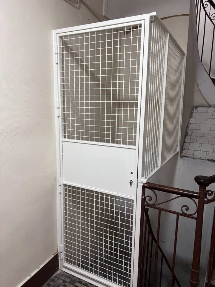 Porte grillagée blanche fermant un accès dans une cage d’escalier