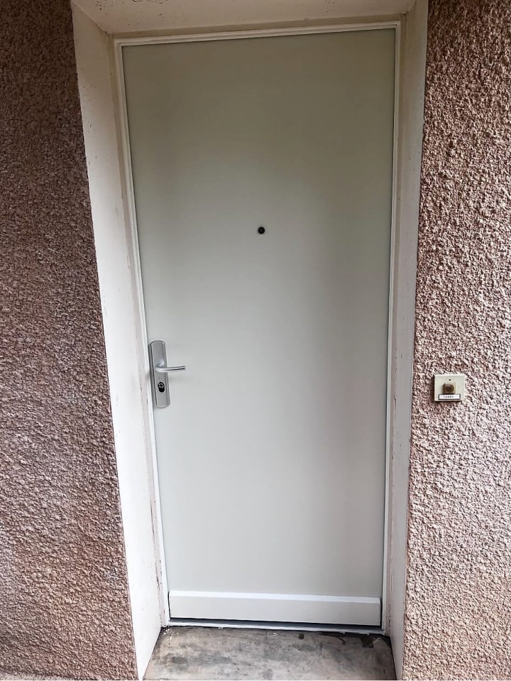 Porte d’entrée blanche posée en façade, avec poignée et serrure neuves