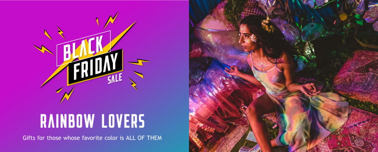 Rainbow lovers gift guide. Brunette girl wearing a rainbow mesh sleeveless maxi dress with flowers and glitter sitting in darkly lit colorful room.