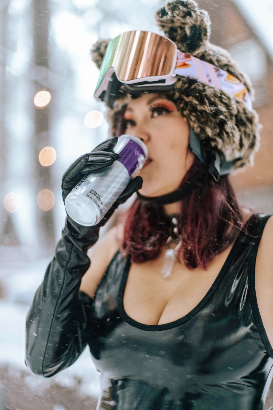 A girl in a leopard ears ski helmet takes a sip of Psychedelic Water outside in some snow showers.
