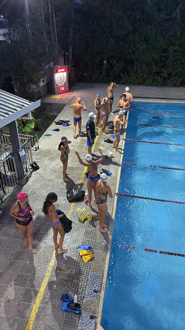 Grupo de nadadores preparándose para para entrar al agua, mientras el entrenador observa