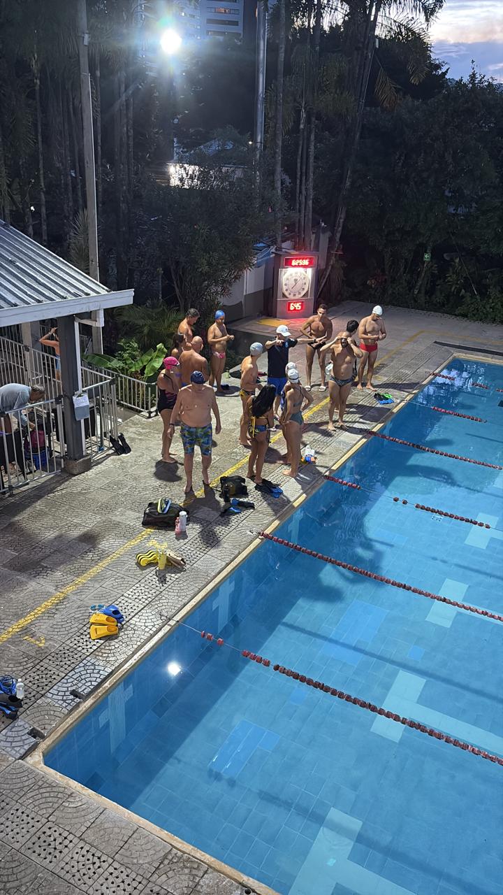 Grupo de atletas a pie de piscina, preparados para entrar a la piscina, con el entrenador observando el inicio del entrenamientos