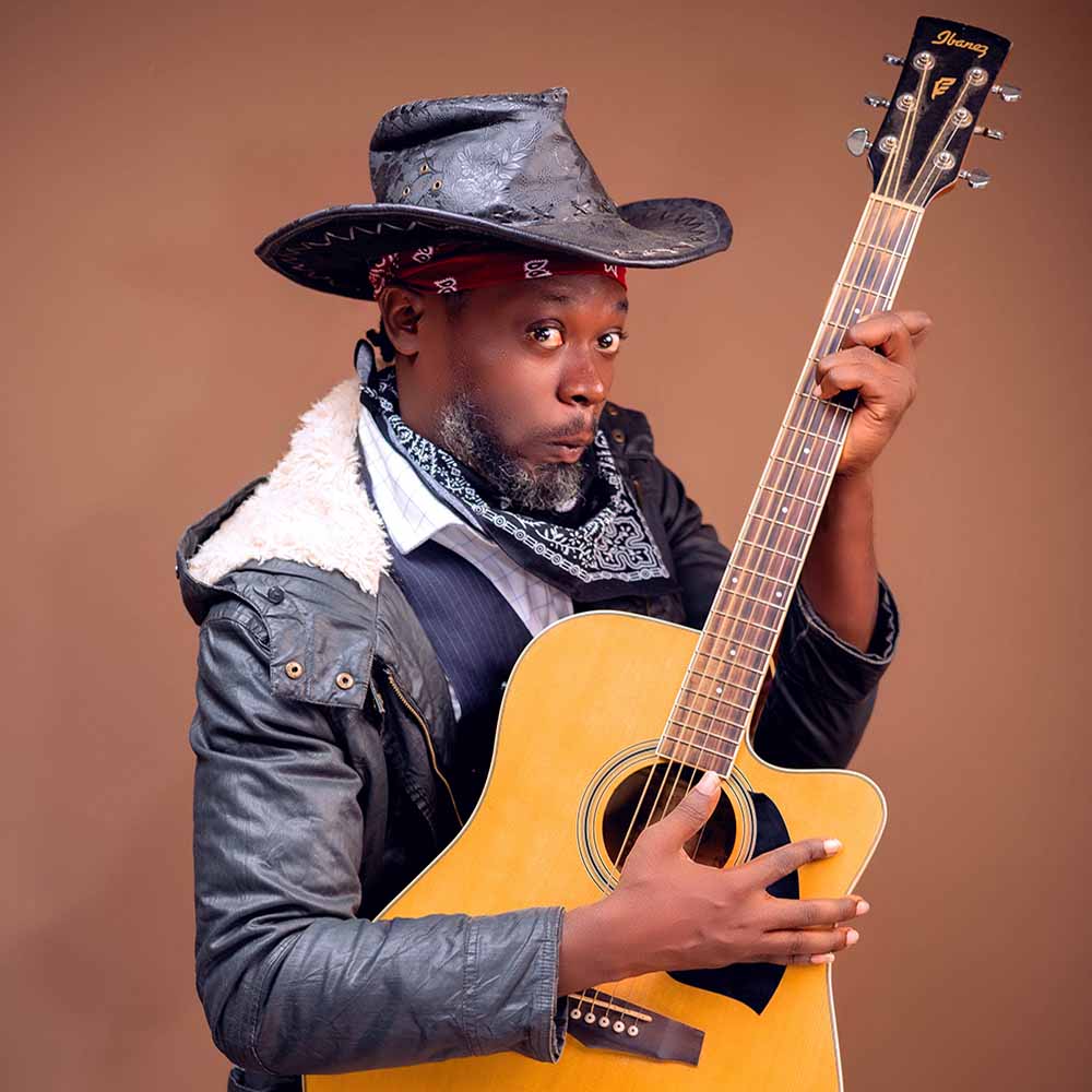 Joe Kuntani holding an acoustic guitar in a black cowboy hat and bandana.