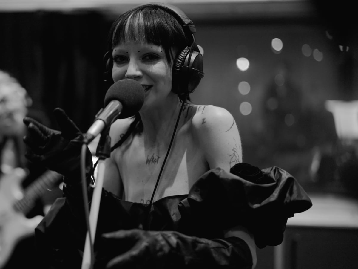 Bambie Thug smiling at the microphone with the band playing behind them