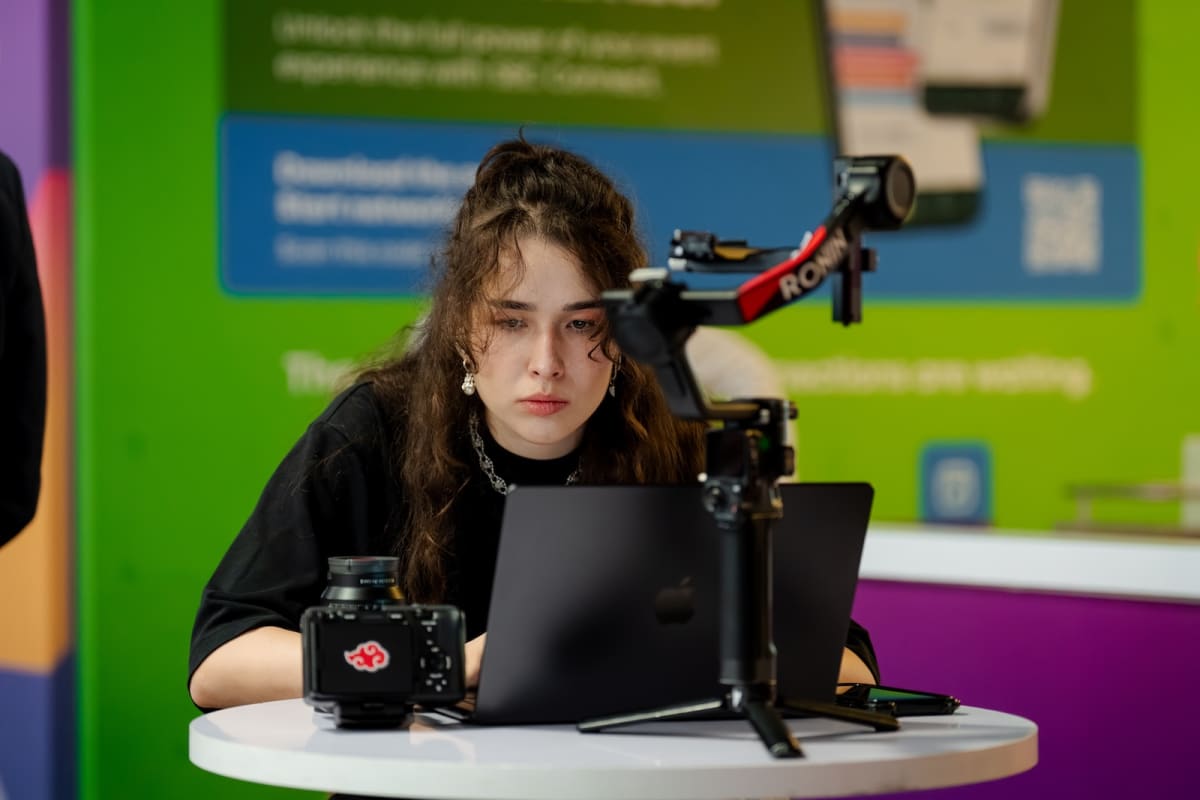 Violet Coretnic editing on a laptop beside a camera rig at a trade show stand