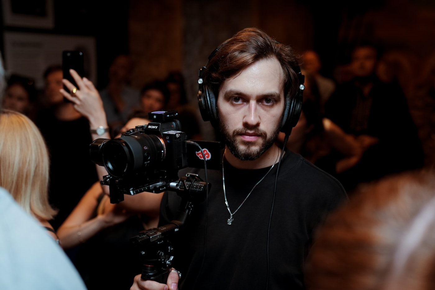 Vitalii Vakulchuk mid-shoot in a crowded event, headphones on, filming with a Sony camera on a gimbal