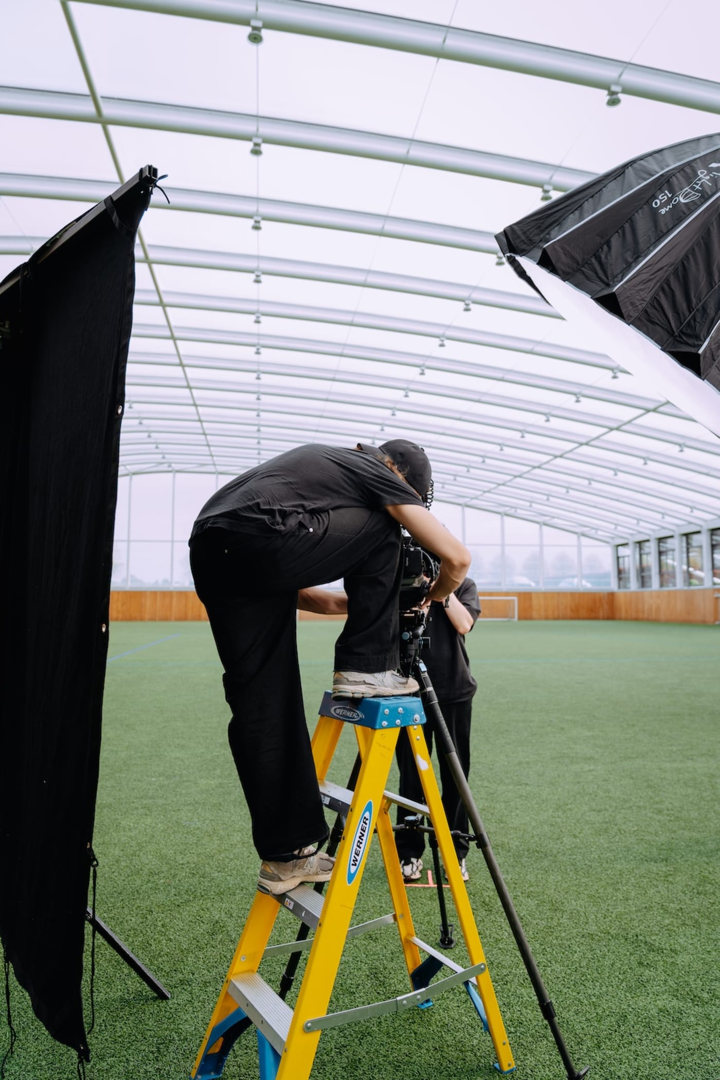 A We Stream camera operator on a stepladder setting up a shot on an indoor football pitch