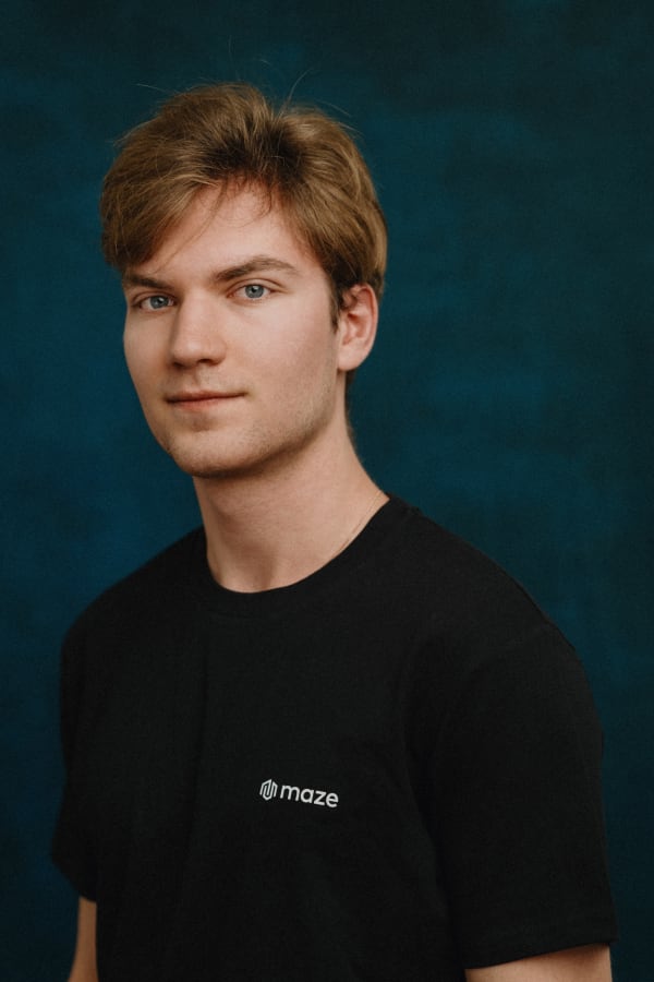 A Maze team member in a branded black t-shirt, photographed against a teal backdrop at the company offsite.
