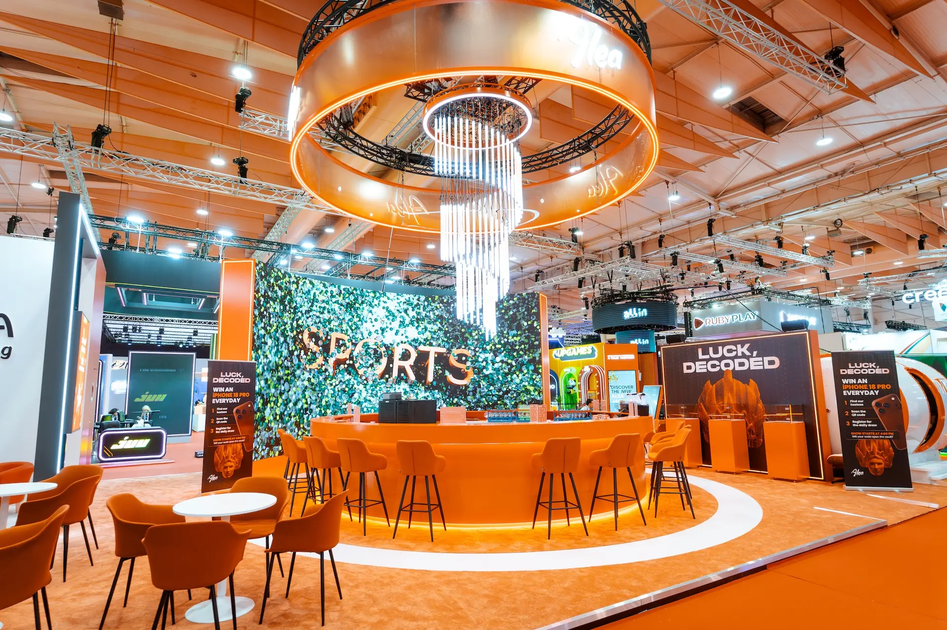 Alea stand B213 at SBC Summit Lisbon 2026 before doors opened: orange bar, chandelier and the Luck, Decoded raffle wall