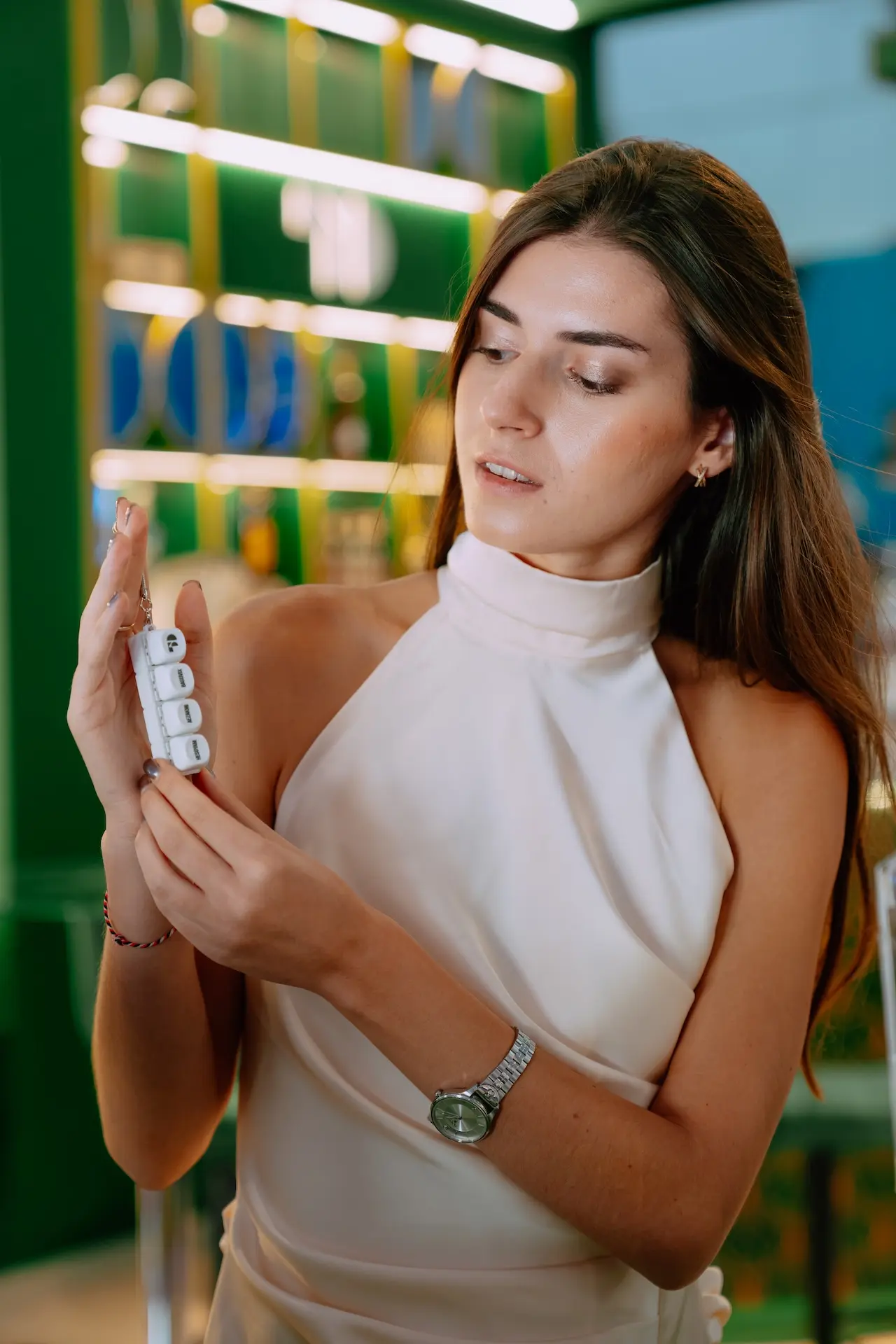 A 50 Partners hostess in a white halter dress looking at the branded dice keychain, shot in a quiet moment on stand F441, SBC Summit Lisbon 2026