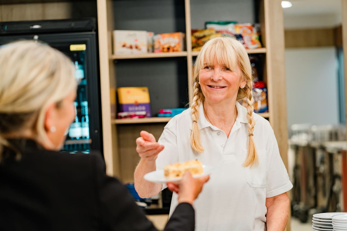 Mitarbeiterin reicht ein Stück Kuchen in der Cafeteria