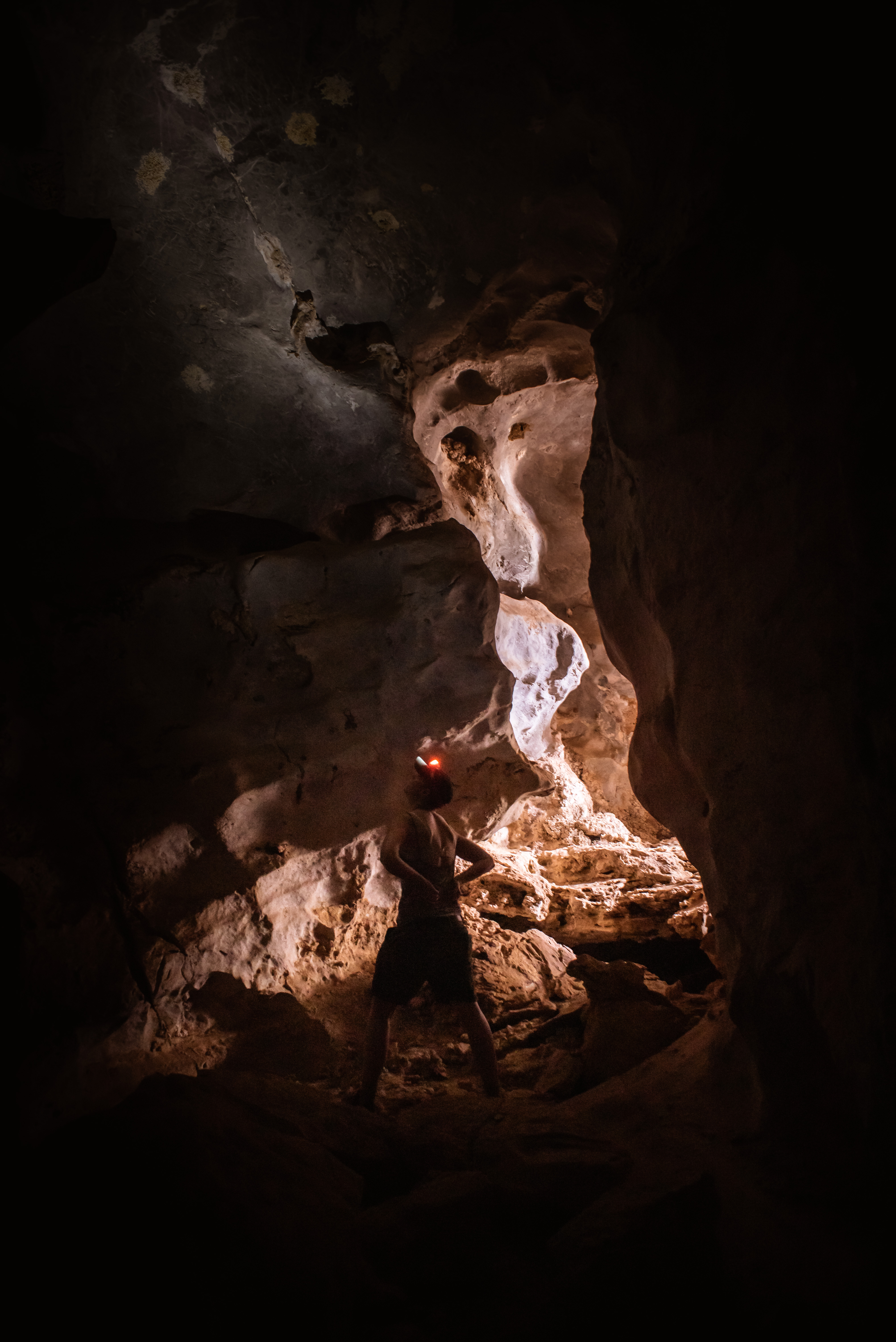 woman stands in cave and sunlight shines from the entry behind
