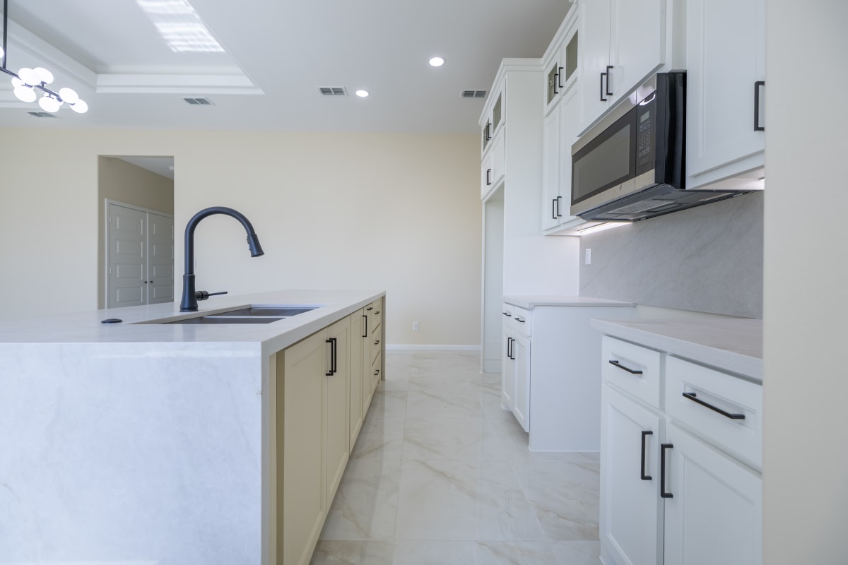 Kitchen with a quartz island and undermount sink, white shaker cabinetry with matte black hardware, and a stainless steel microwave