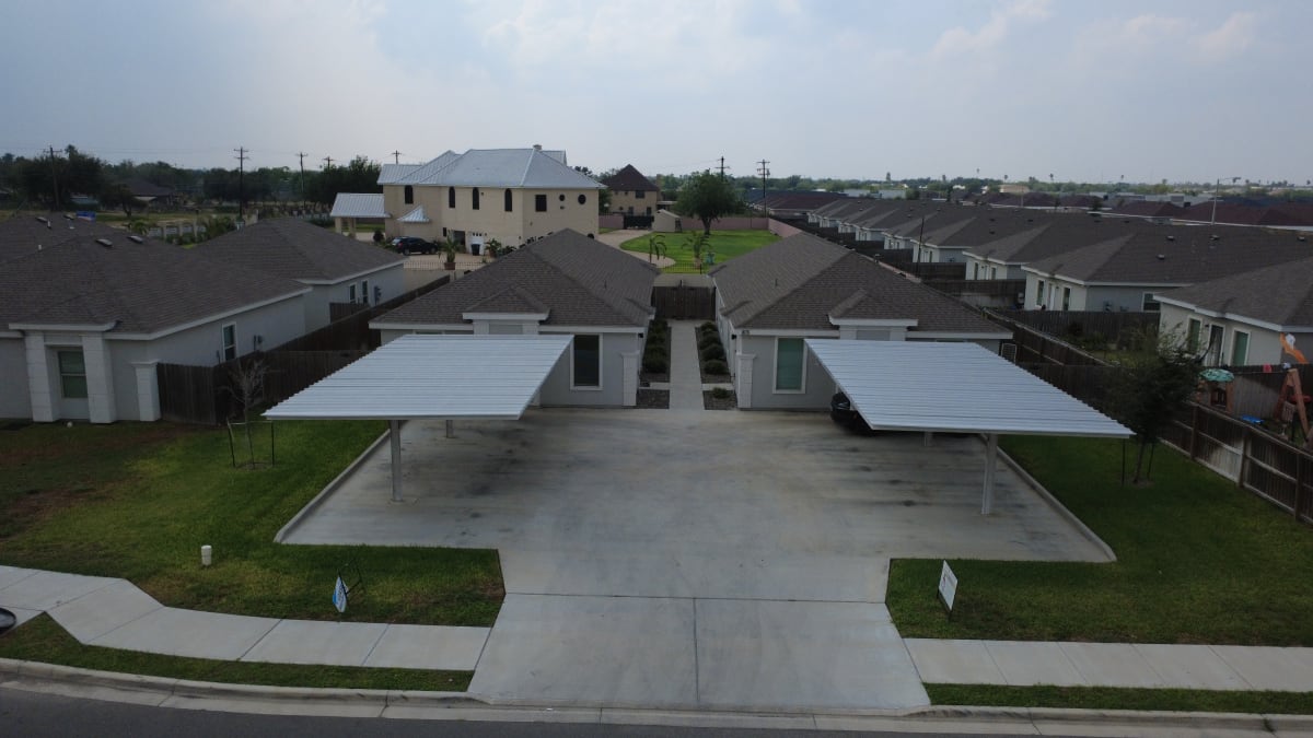 Sunset Valley fourplex in Alton, Texas, seen from the street: two gray stucco wings with a central walkway and a covered carport on each side