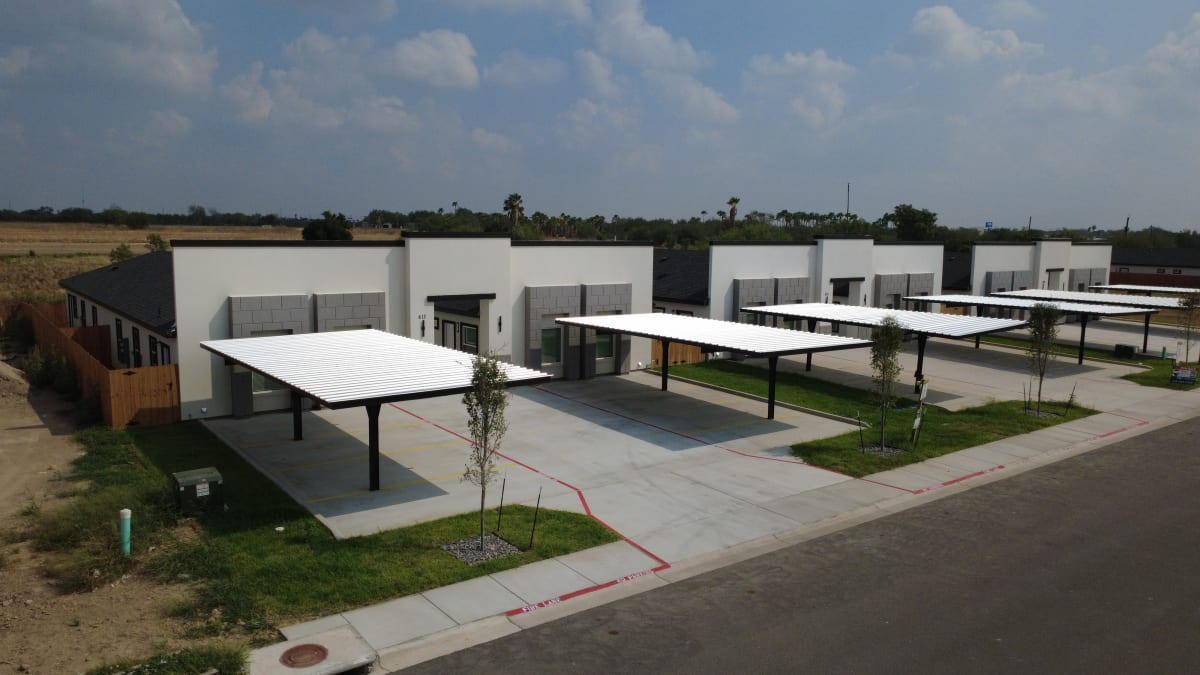 A row of white stucco fourplexes at Trosper Creek, each with gray block accents and a covered carport on either side of the entry