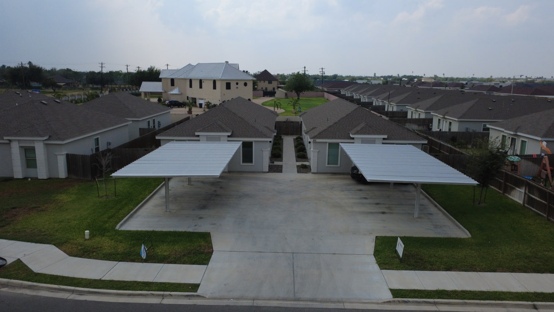 Sunset Valley fourplex in Alton, Texas, seen from the street: two gray stucco wings with a central walkway and a covered carport on each side