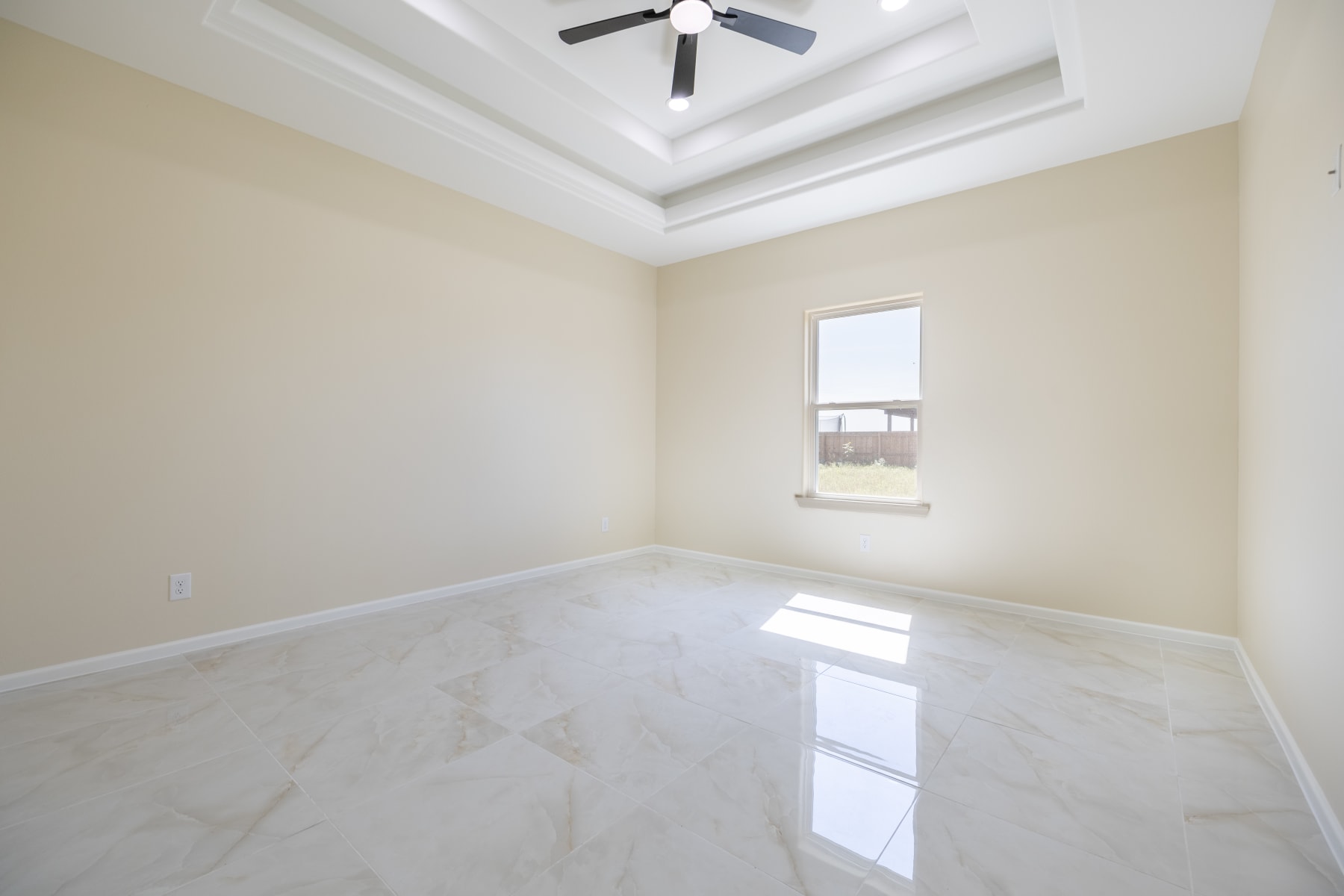 Unfurnished bedroom with a window and a tray ceiling with a fan
