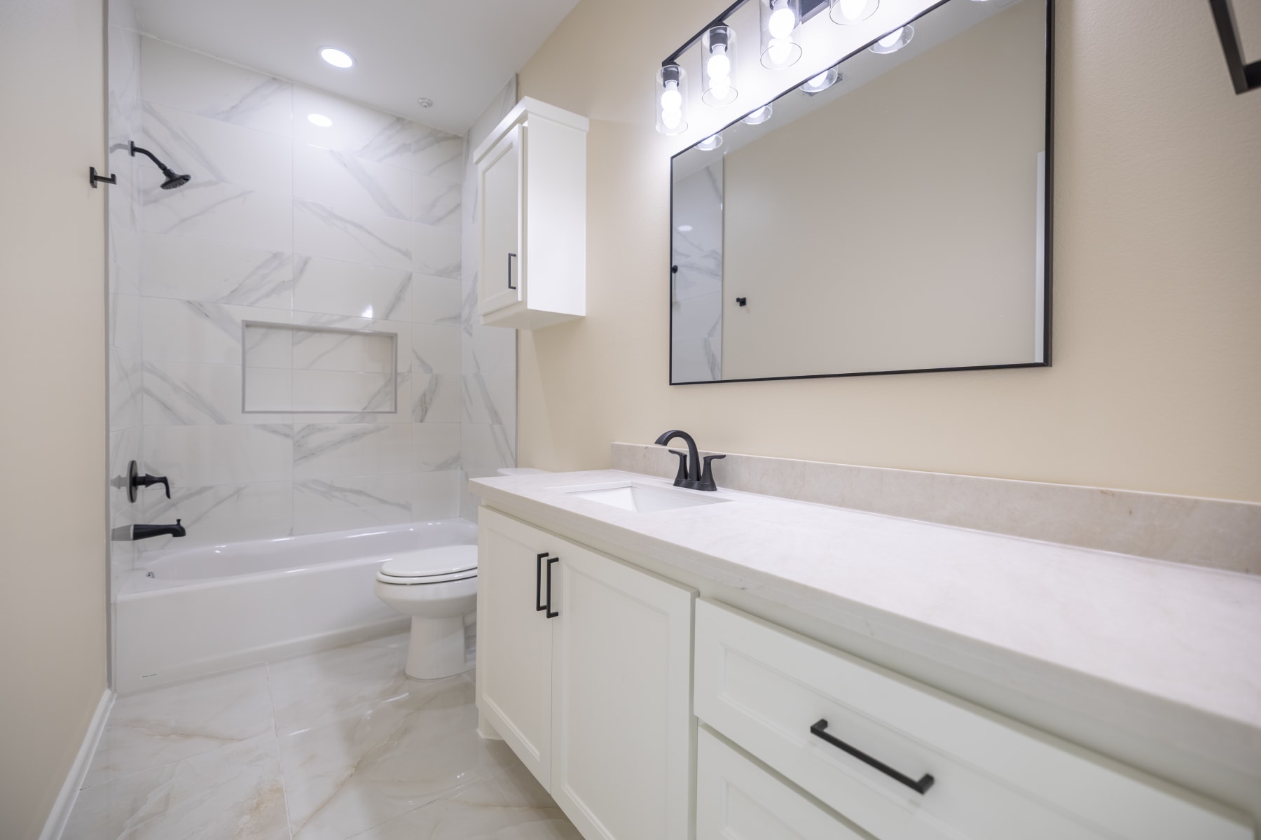 Secondary bathroom with a marble-tiled tub and shower, single vanity and matte black fixtures