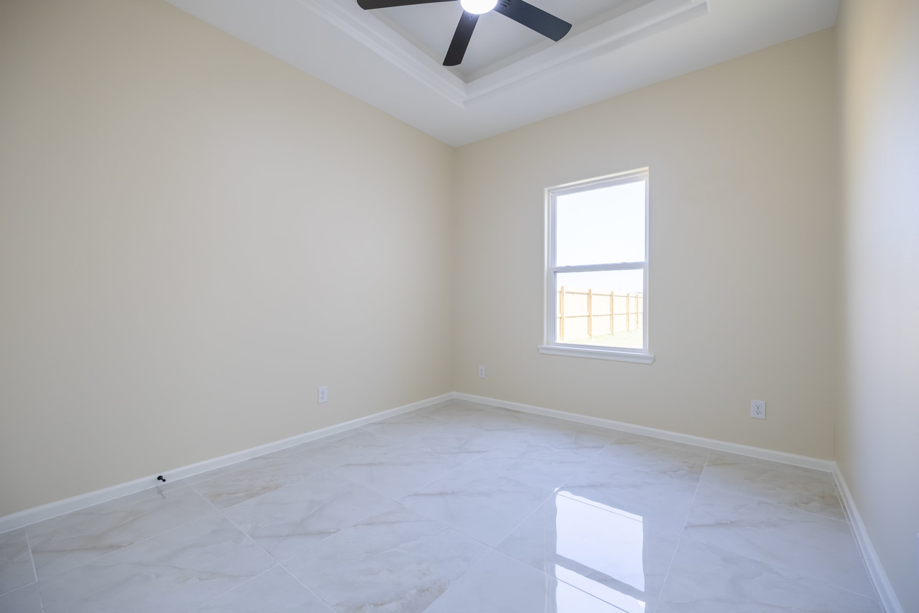 Unfurnished bedroom with a window, tray ceiling and ceiling fan