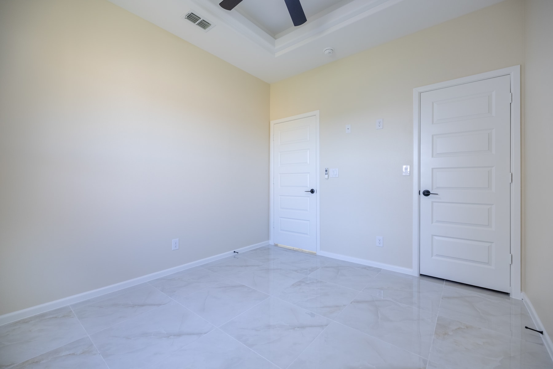 Unfurnished bedroom with two panelled doors and a tray ceiling fan