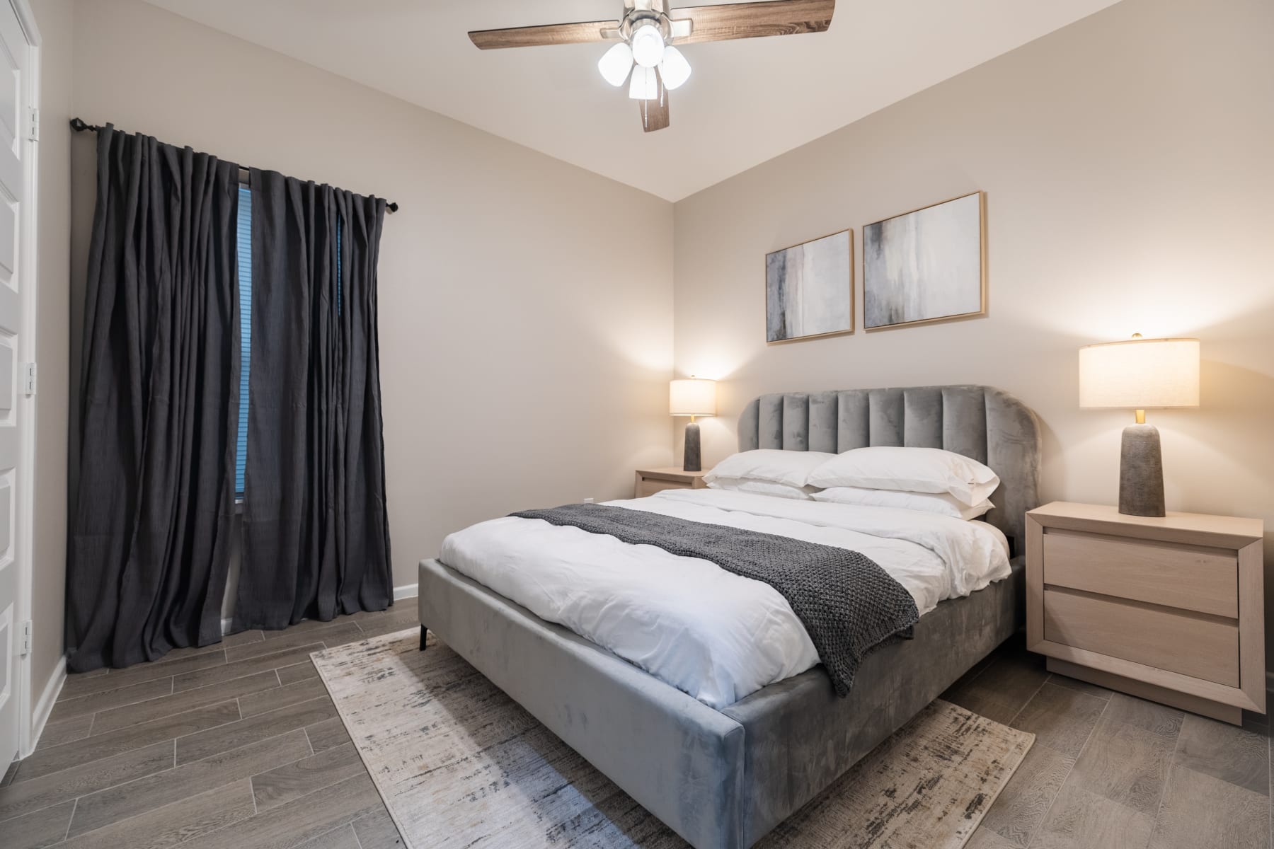 Staged bedroom with upholstered headboard, dark curtains, and matching nightstand lamps at Westwood Villas