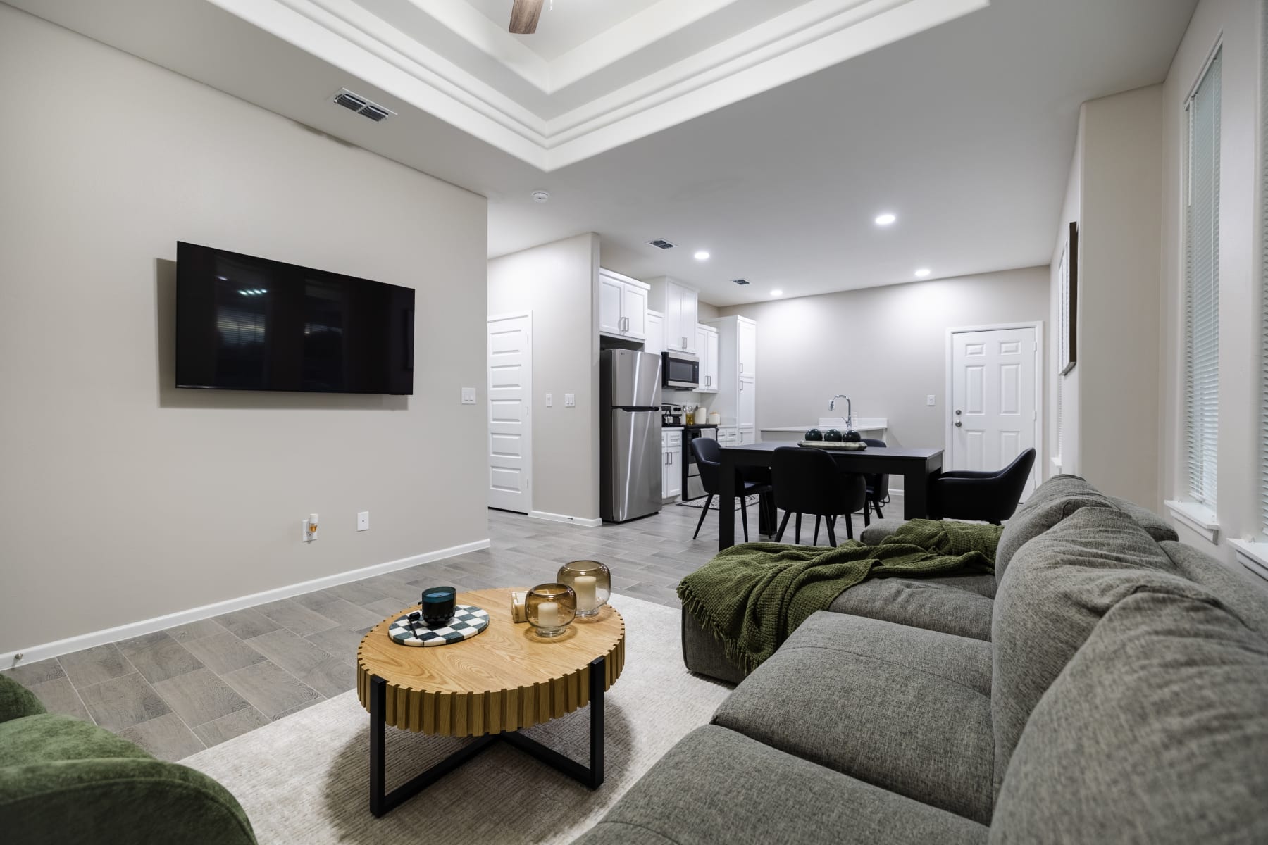 Staged living room with wall-mounted TV, sectional sofa, and open kitchen in the background at Westwood Villas