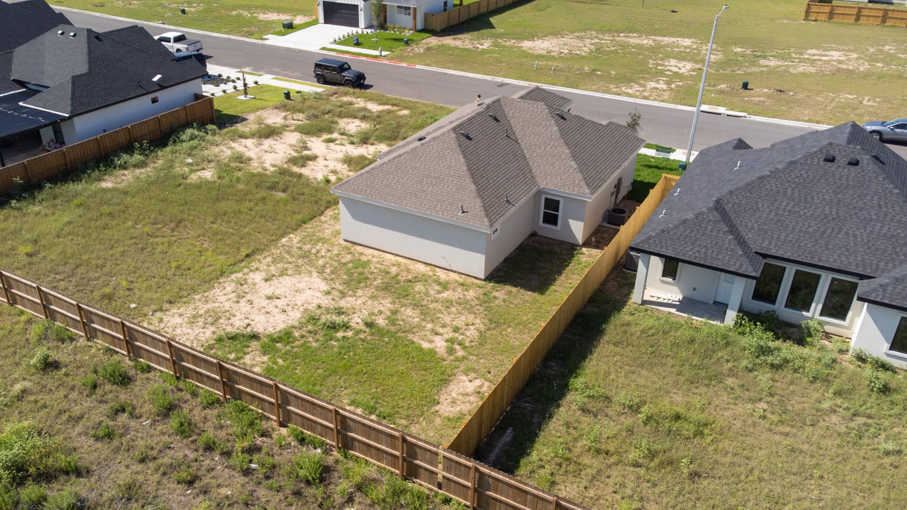 Aerial view of a completed home with its fenced yard and open land alongside