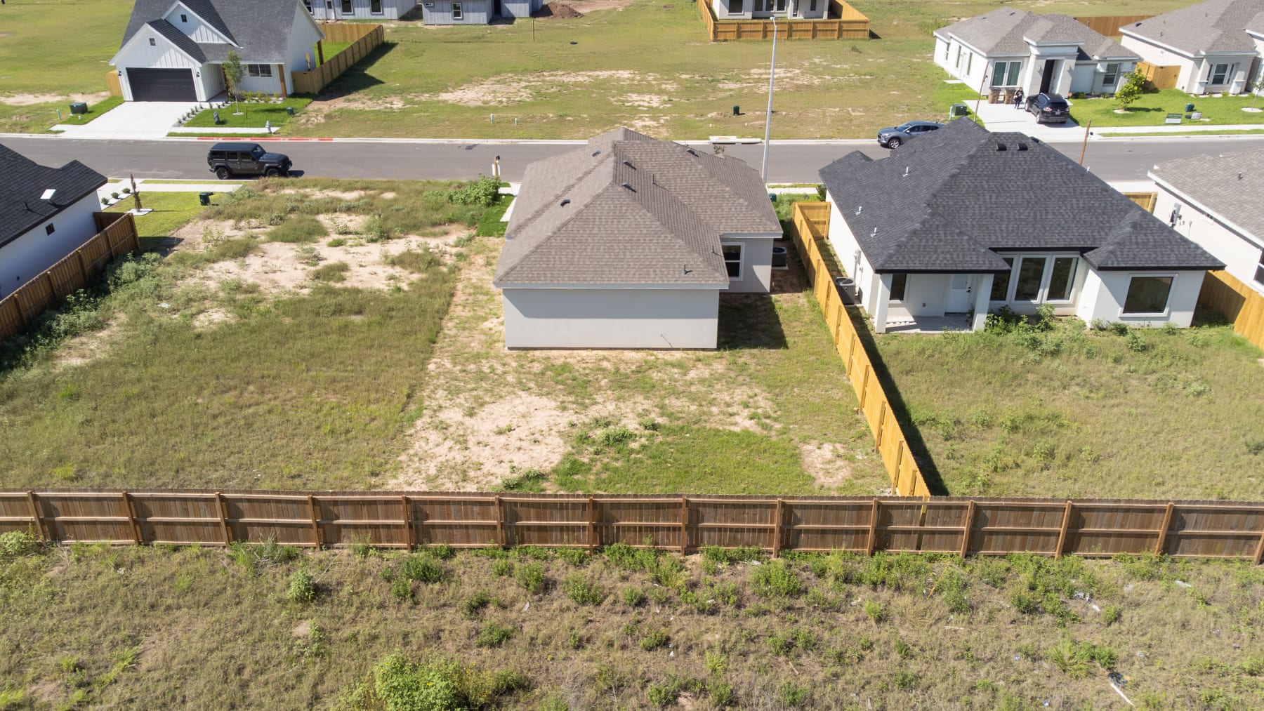 Aerial view of the rear of the home and its wood-fenced back yard