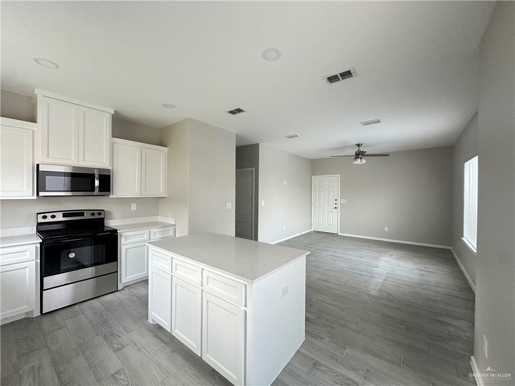 Vida kitchen with white shaker cabinets, a center island and stainless range and microwave, open to the living room