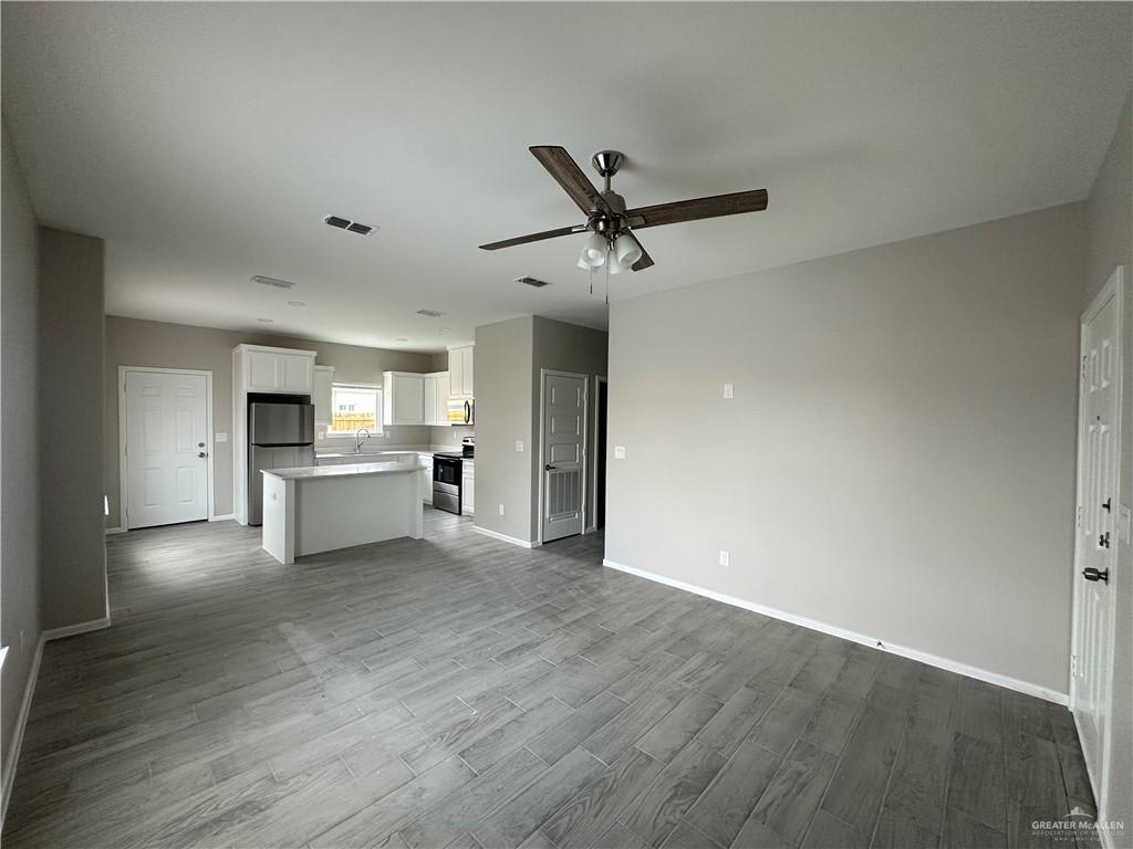 Vida open living area with the kitchen and front door beyond, wood-look tile throughout