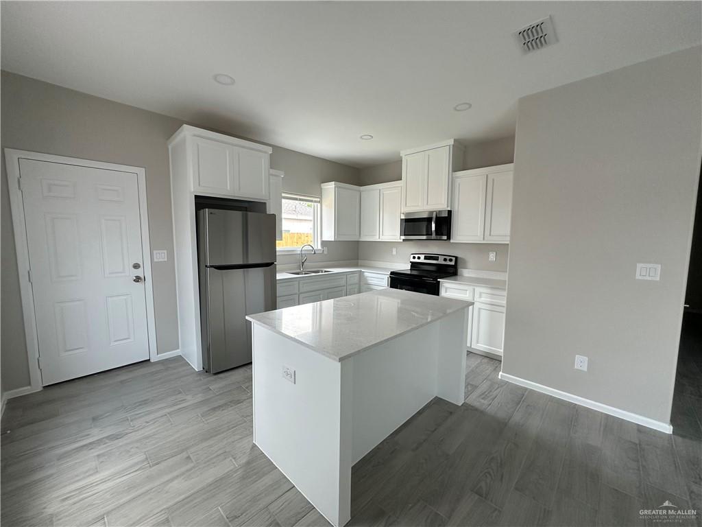 Vida kitchen with a quartz-topped island, stainless refrigerator and a window over the sink