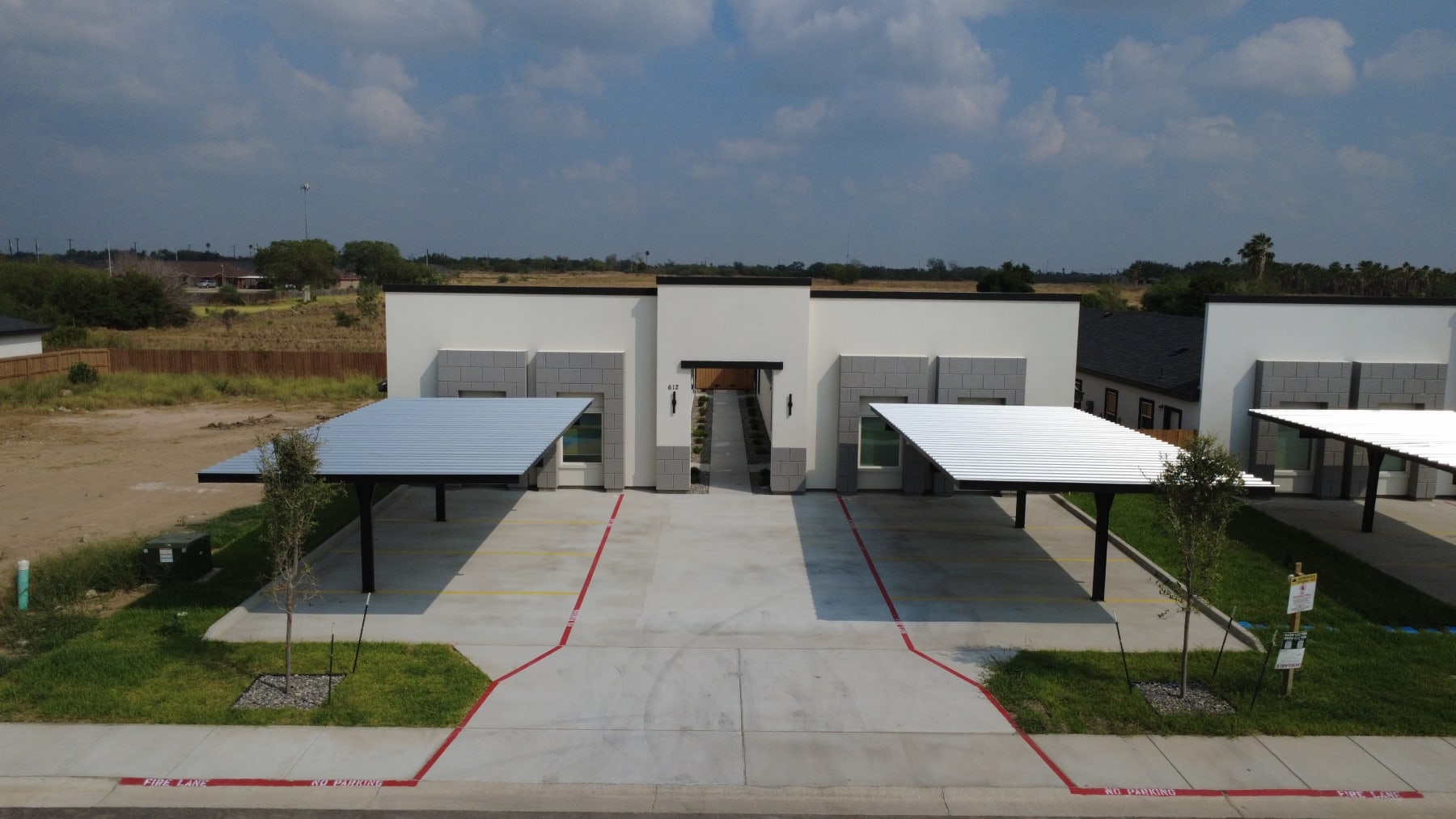 A fourplex from across the street, with a covered carport on each side of its breezeway entry and open land behind