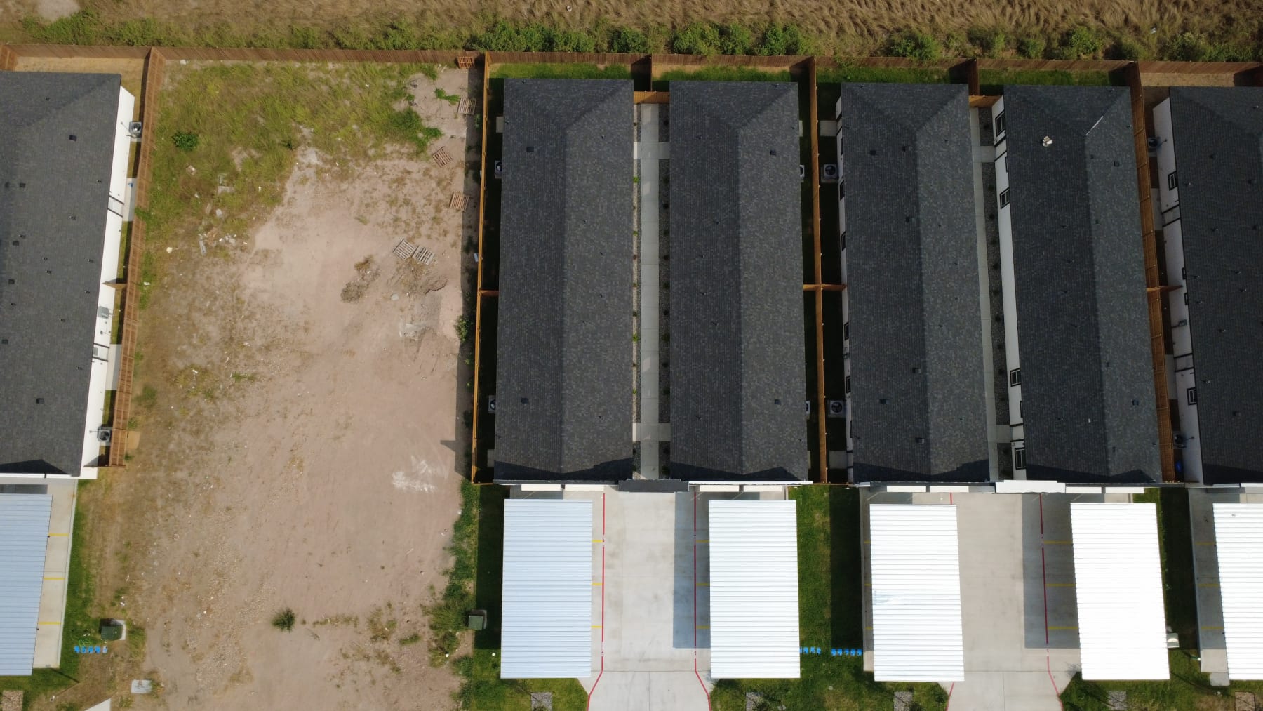 Overhead view of fourplex roofs in a row, with their carports along the street and an open homesite beside them