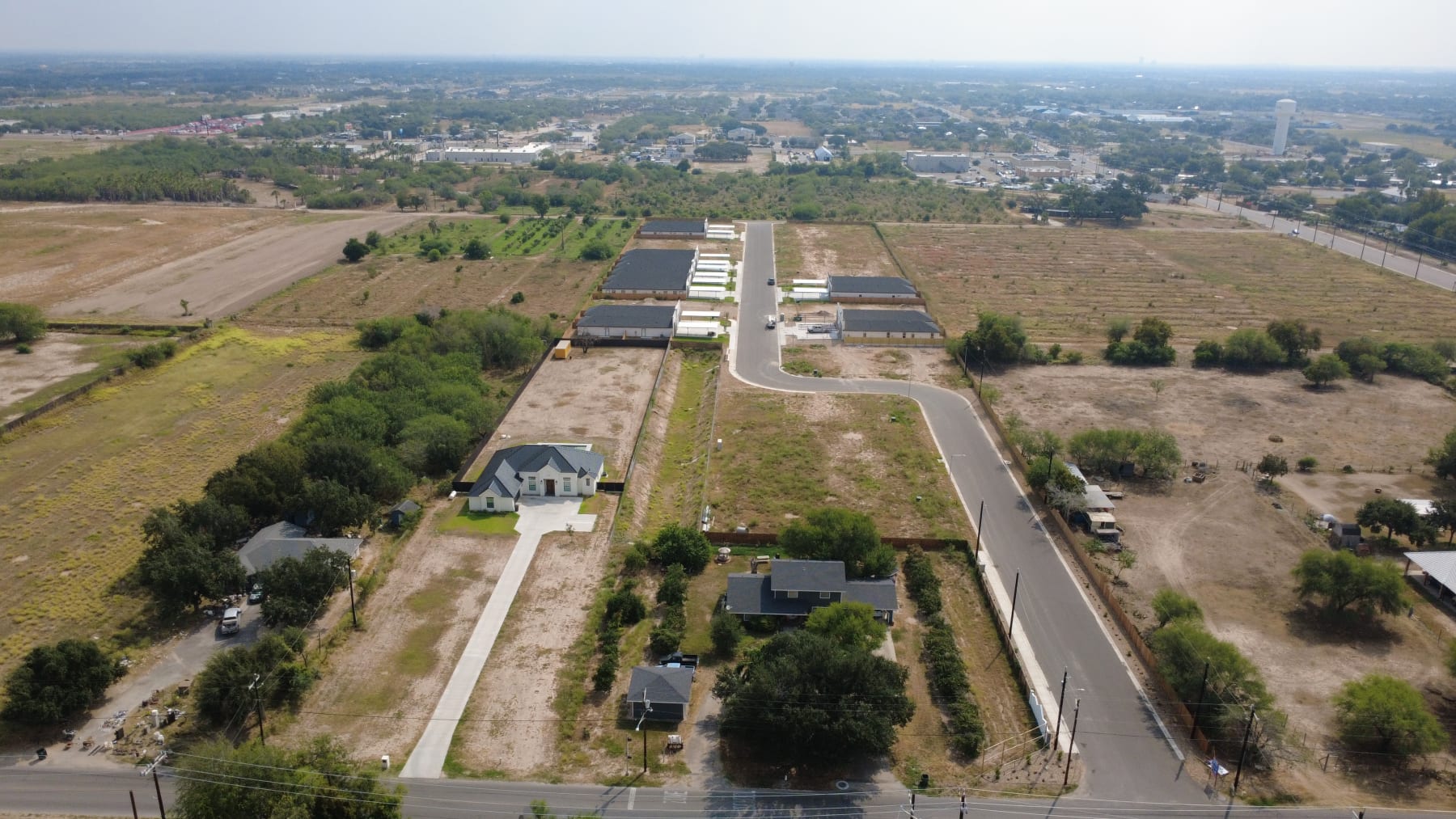 High aerial view with Trosper Creek's fourplexes in the middle distance, along a street that curves in from the main road