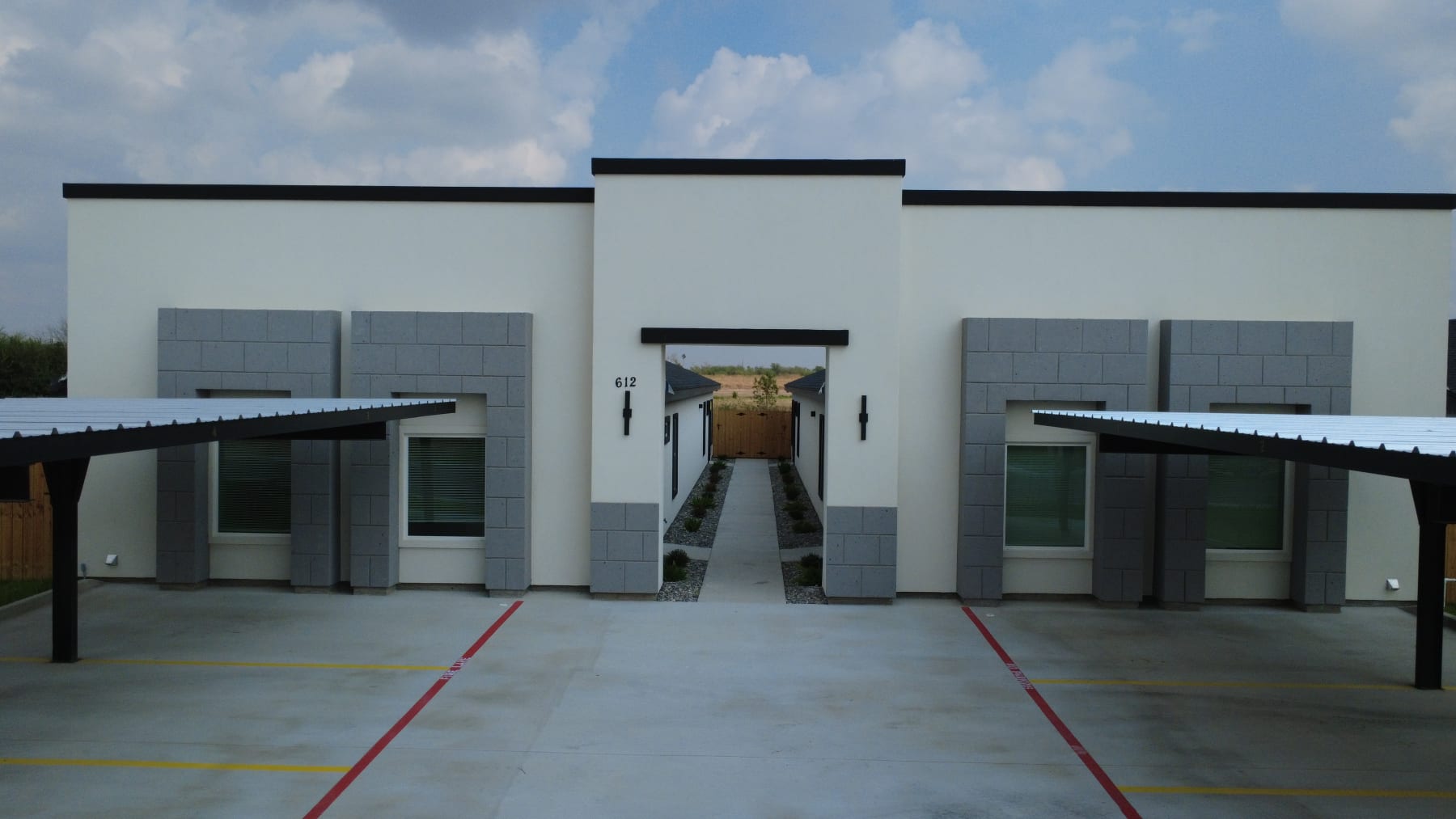 The breezeway entry of a fourplex between its two wings, framed by gray block and covered parking