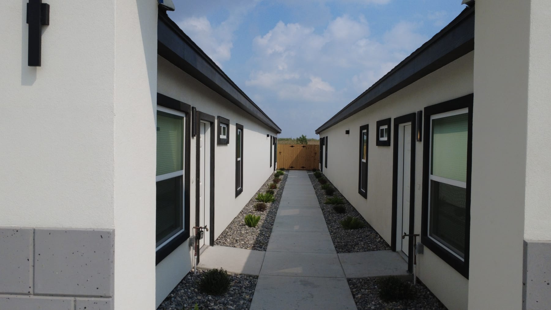 The breezeway between a fourplex's two wings: a concrete path through gravel beds and low plantings to a wood gate