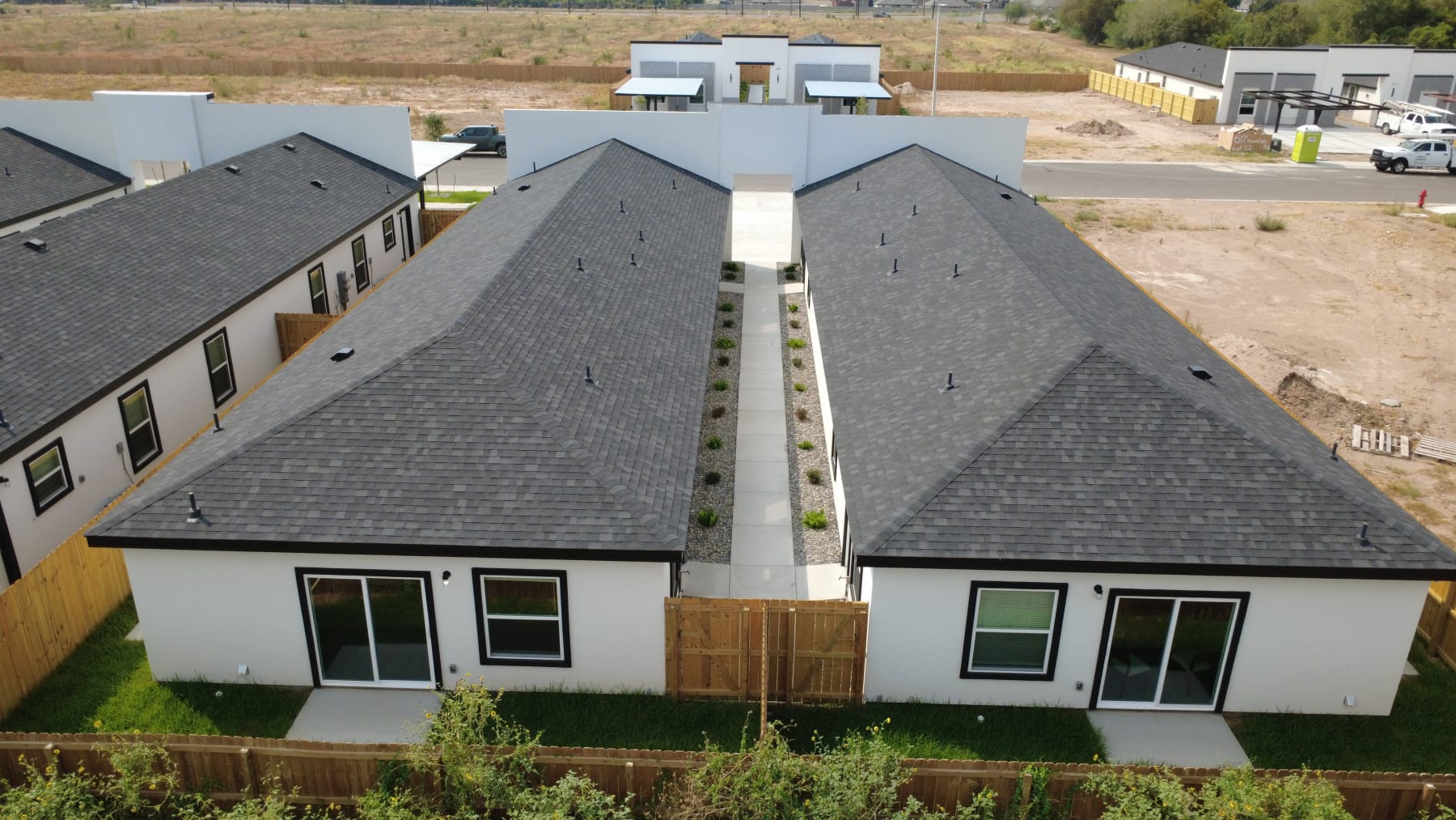Rear of a fourplex from above: two hipped-roof wings, a planted breezeway, sliding patio doors and wood-fenced yards