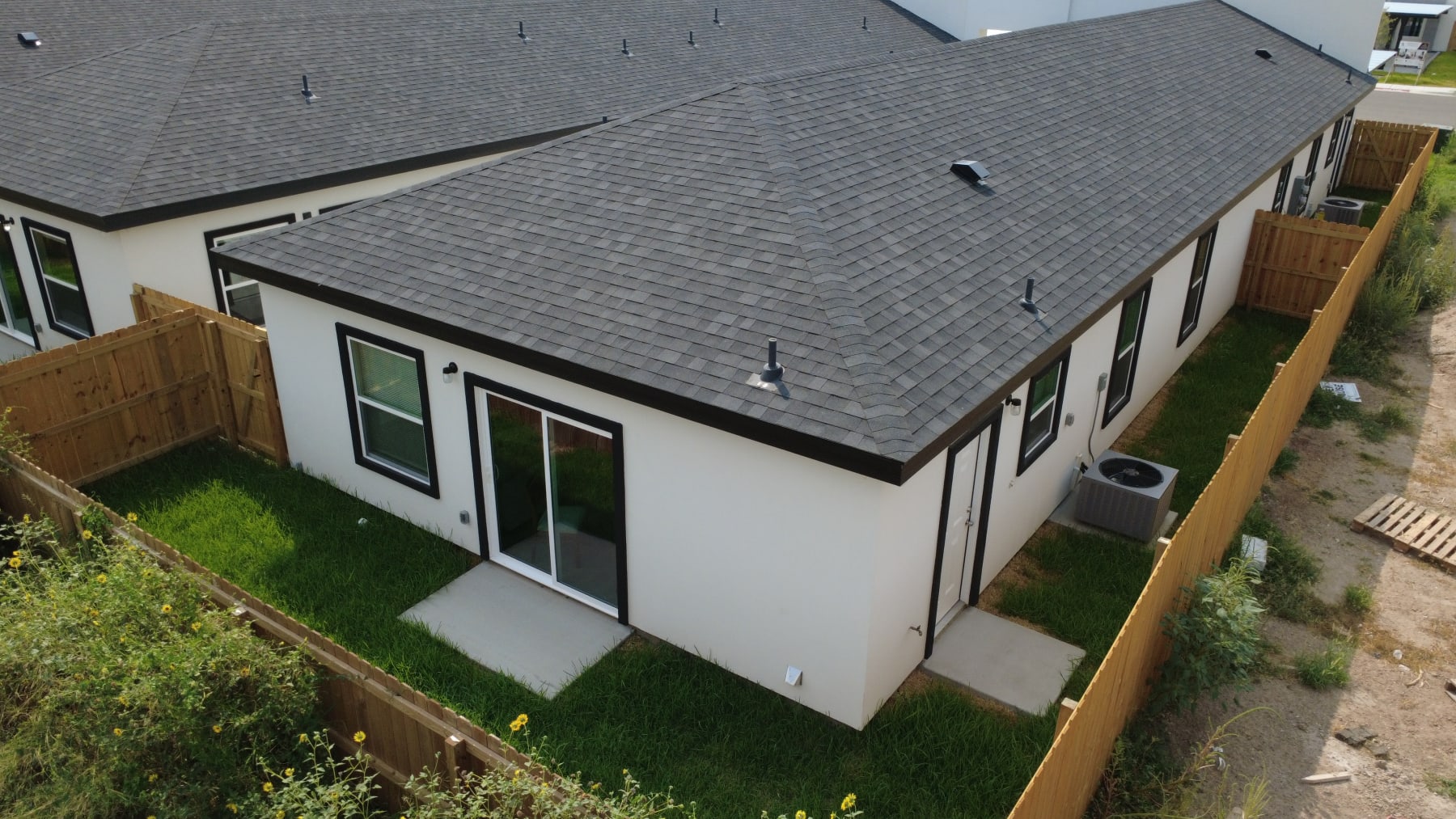 A fenced back yard with a lawn, a sliding patio door and a concrete pad