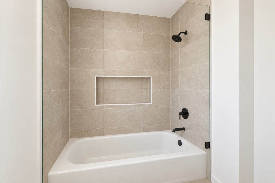 Rendering of the 431 Padre hall bath tub and shower, tiled in Phoenix Sand with a recessed niche and black shower trim.
