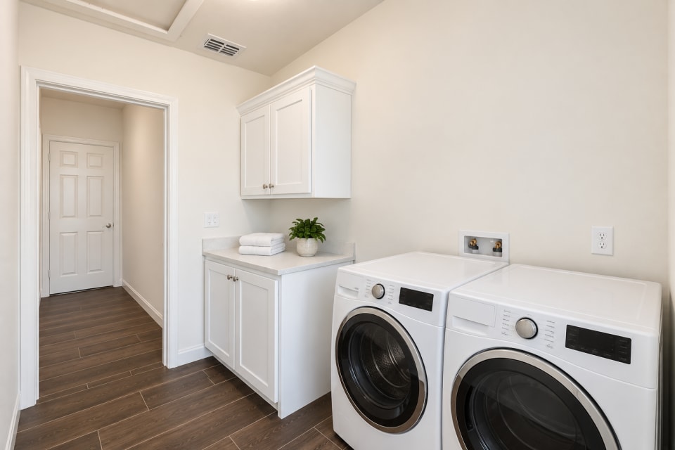 Rendering of the 433 Padre laundry room with Alabaster cabinets, a Pebble White quartz counter, a washer and dryer, and dark wood-look tile floors.