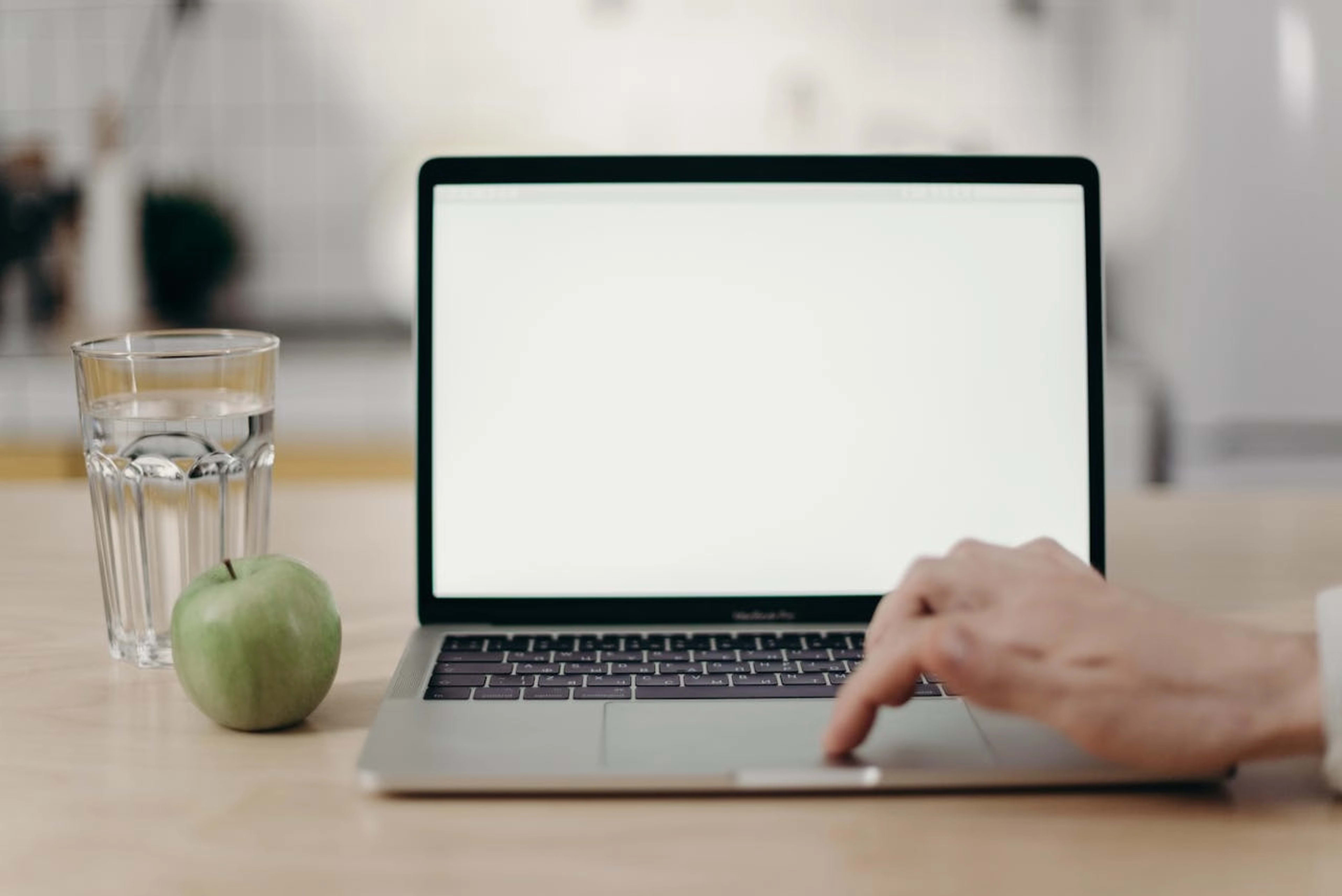 Laptop előtt dolgozó kéz, mellette egy zöld alma és egy pohár víz, a tudatos és zavartalan digitális munka szimbólumaként.