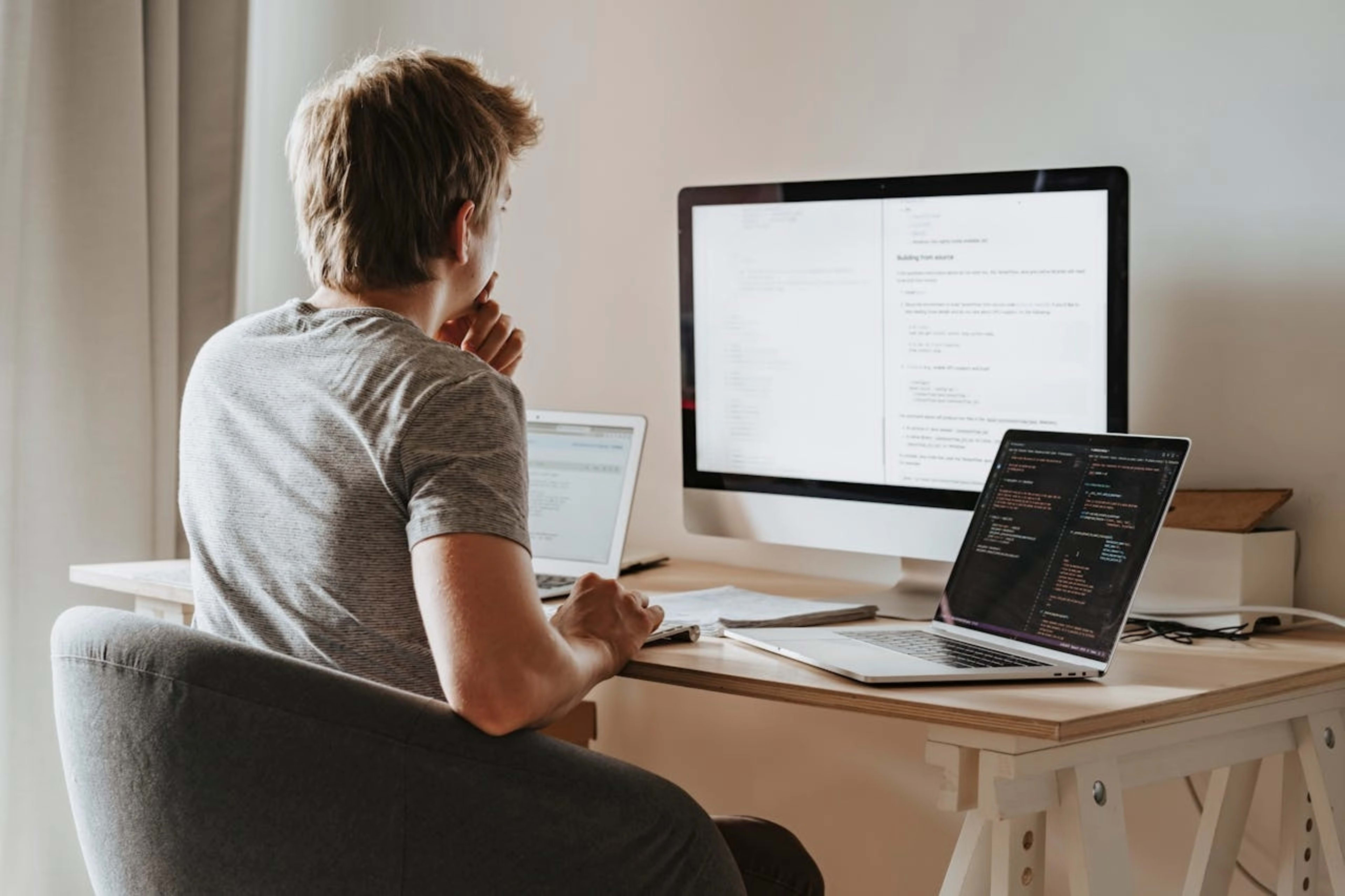 Háttal ülő programozó férfi egy minimalista munkaállomás előtt éppen tanul programozni, szimbolizálva a Pluralsight platformon történő online tanulást.