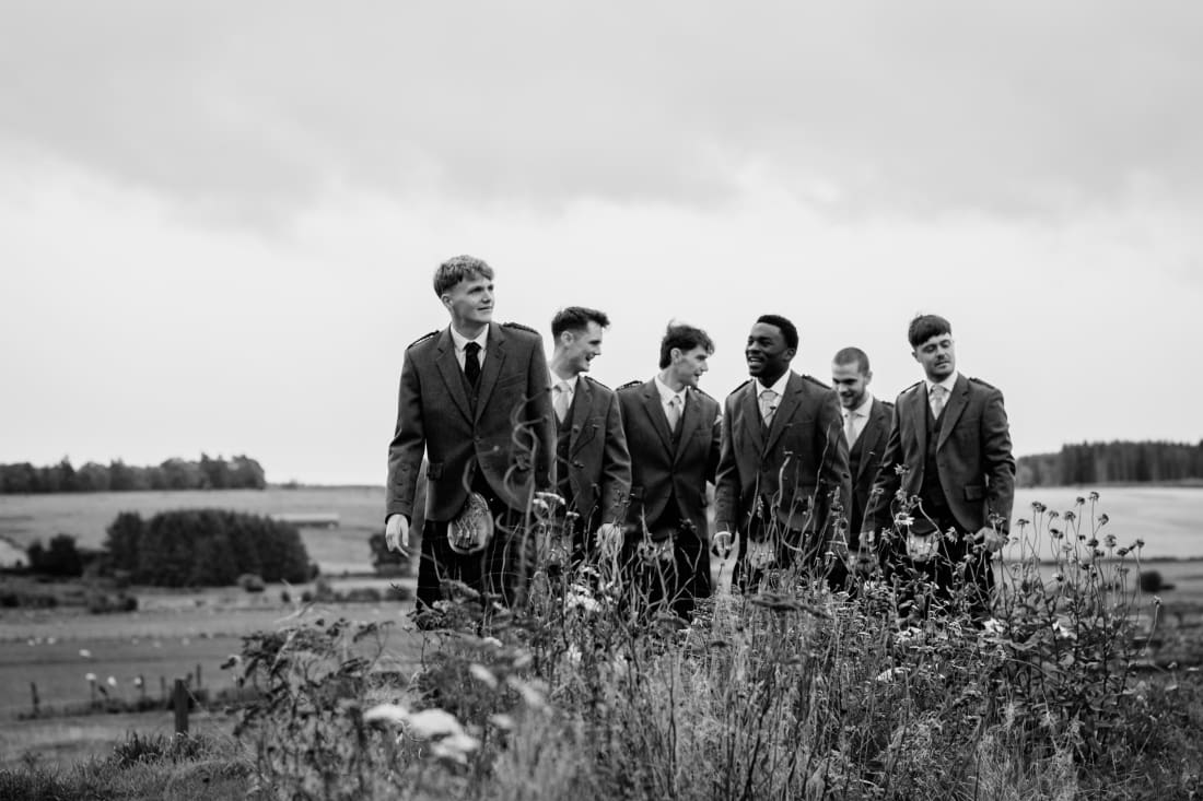 Nathan and his groomsmen stand in the long grass above the fields
