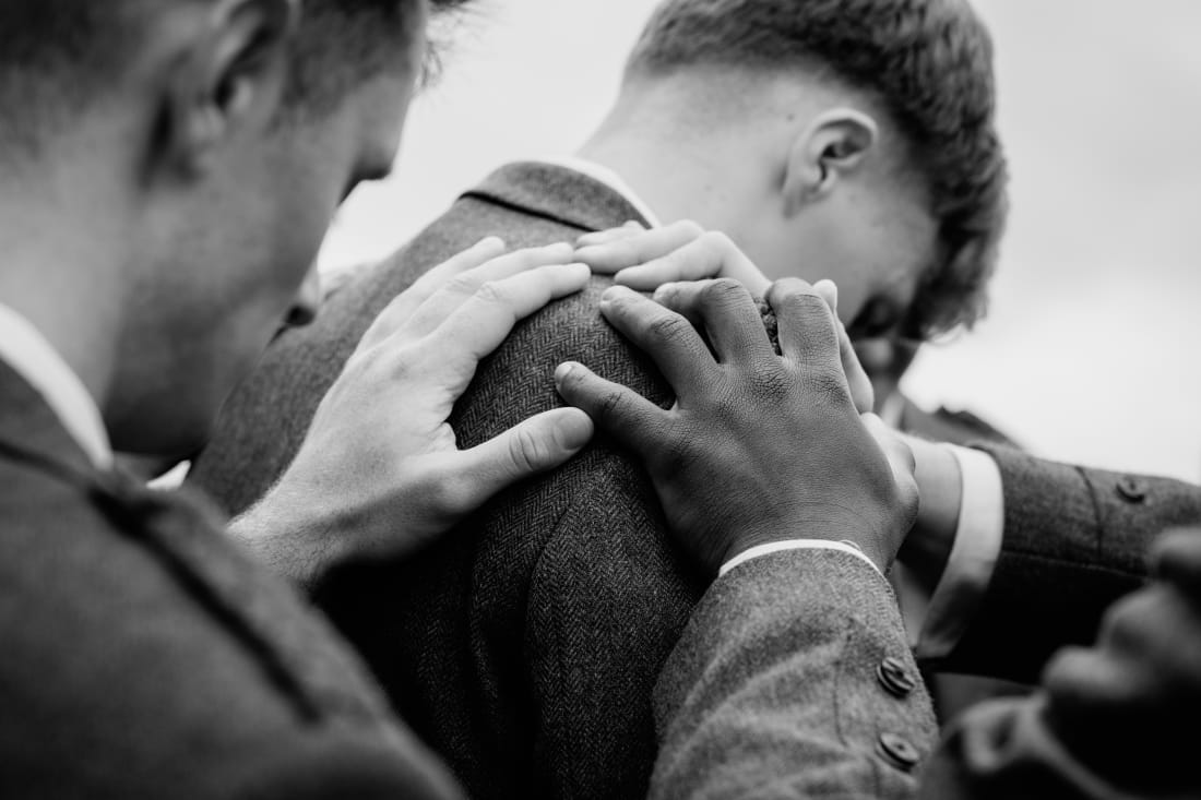 Hands rest on Nathan’s shoulders as he bows his head